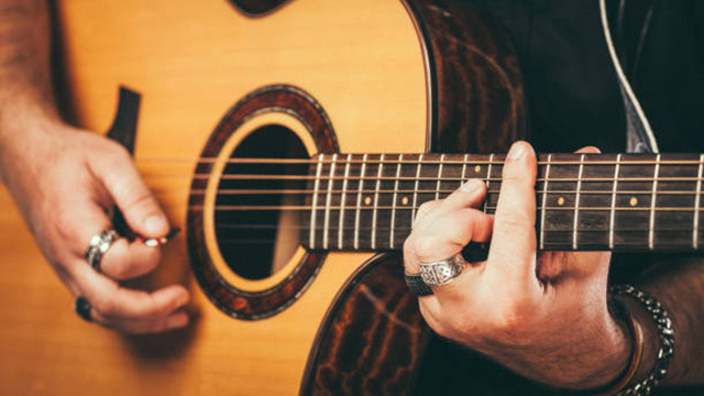 Man playing barre chord on an acoustic guitar